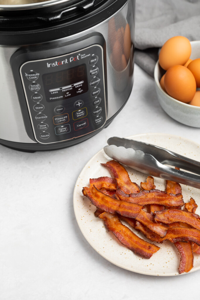 a plate of bacon in front of an instant pot and a bowl of eggs