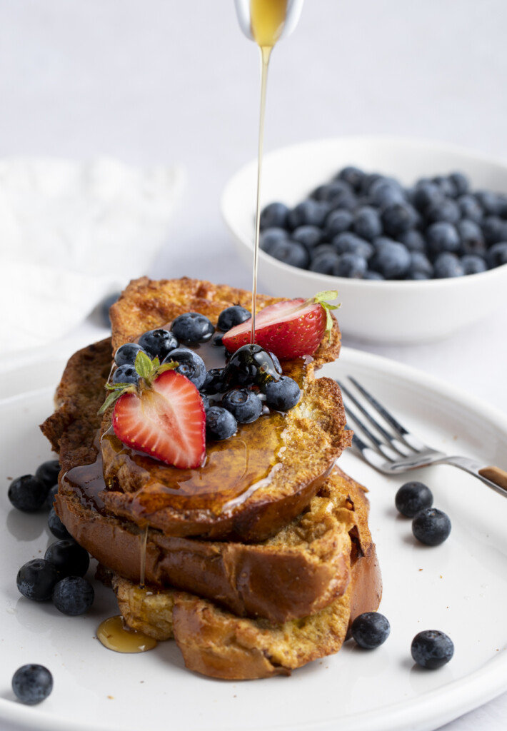 Syrup poured over air fryer french toast on a plate topped with blueberries and strawberries