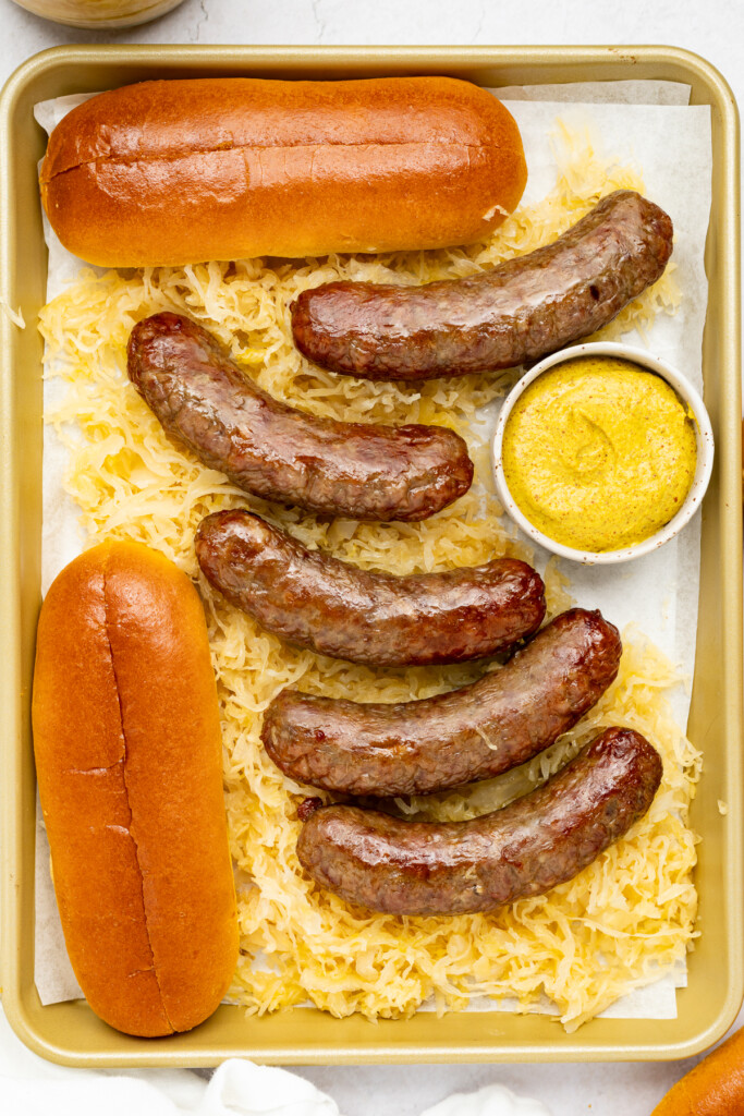 air fryer brats on a baking sheet with saueurkraut, mustard, and buns