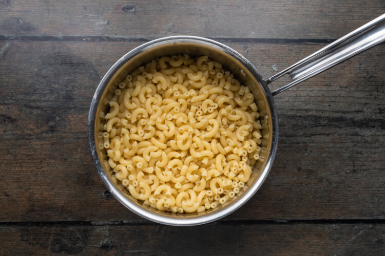 Overhead view of a silver pot holding macaroni noodles on a dark, wooden background.