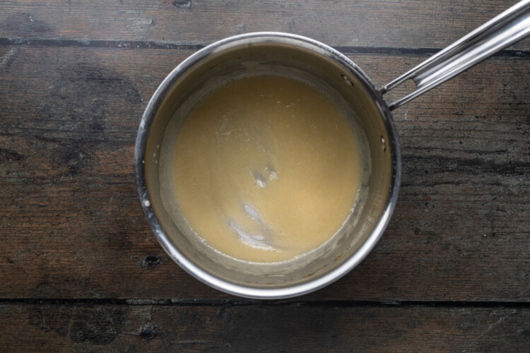 Overhead view of a silver pot of melted butter on a dark wooden background.