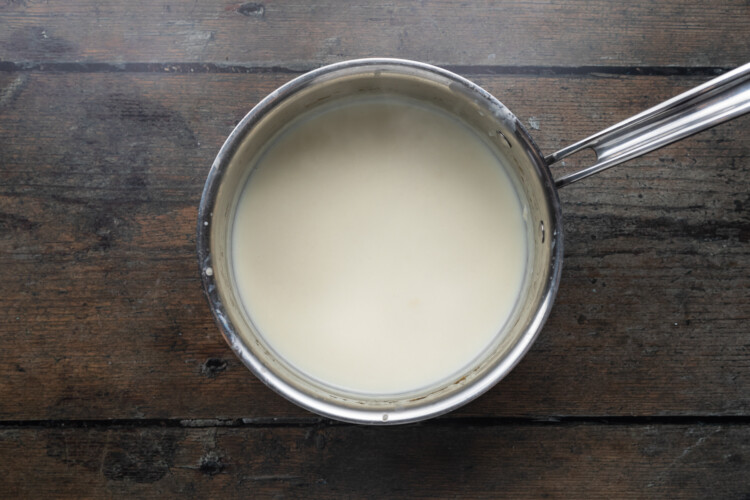 Overhead view of a roux and milk in a silver saucepan on a dark wooden background.