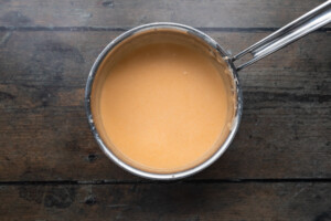 Overhead view of cheese sauce in a silver saucepan on a wooden background.