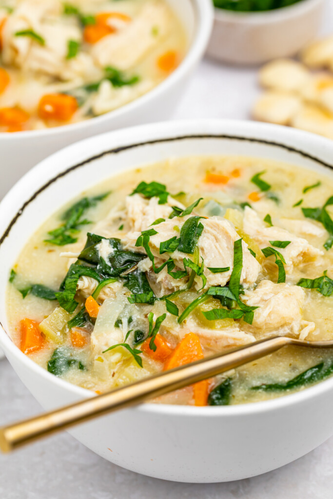 two bowls of chicken florentine soup with crackers and fresh parsley on the side
