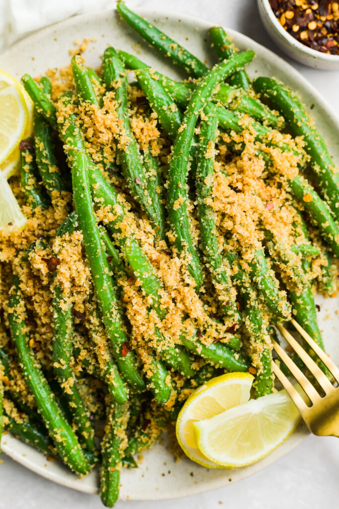 italian green beans on a plate with lemon and red pepper flakes on the side