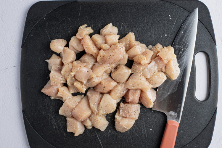 Chopped chicken breasts on a black cutting board with a sharp knife