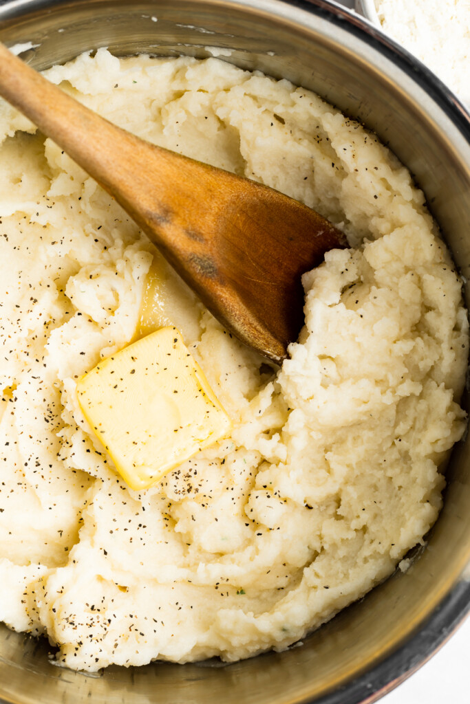 overhead image of mashed potatoes in a pot with butter and a wooden spoon