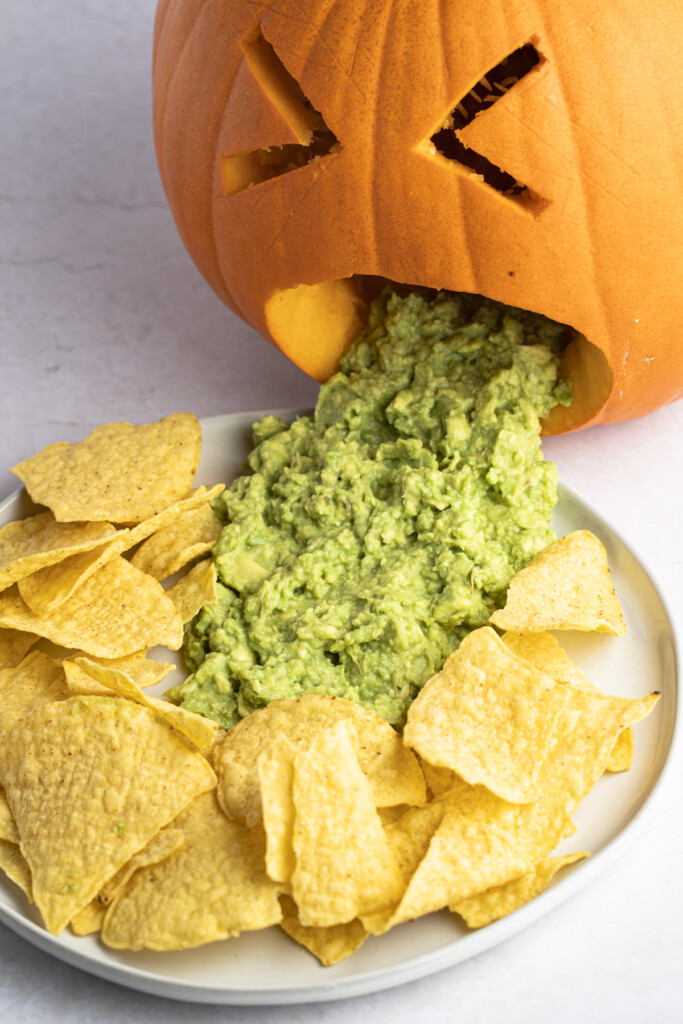 Angled puking pumpkin with guacamole on a plate surrounded by tortilla chips