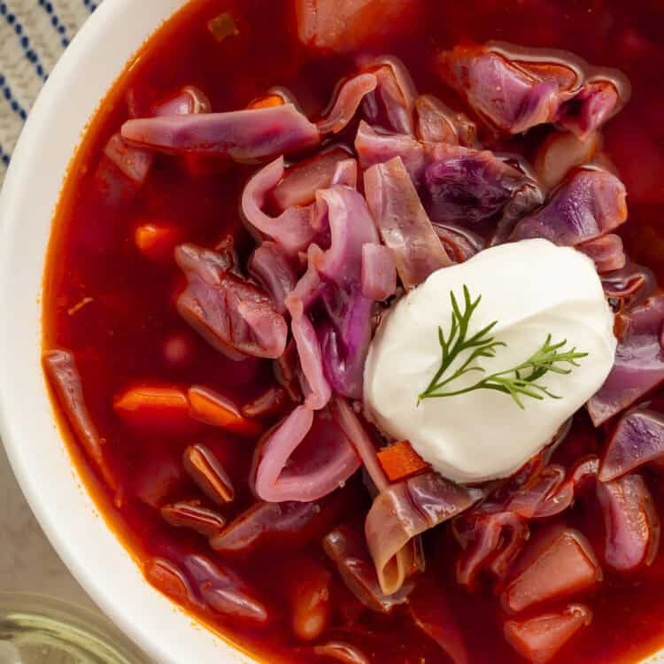 Close up of a bowl of red cabbage soup with a spoonful of sour cream on top.