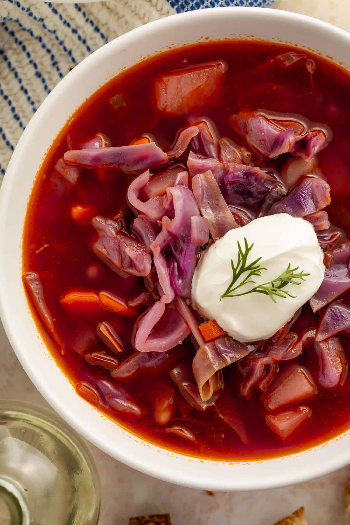 Close up of a bowl of red cabbage soup with a spoonful of sour cream on top.