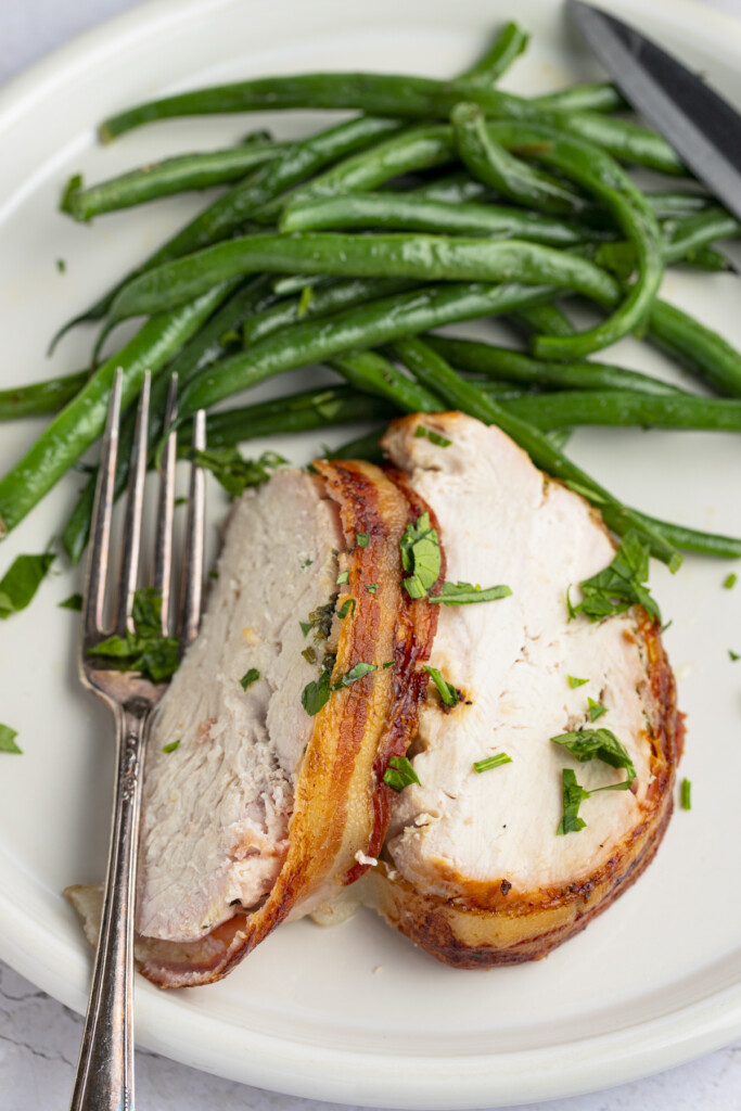 Slices of Bacon Wrapped Turkey Breast on a plate with green beans and a fork