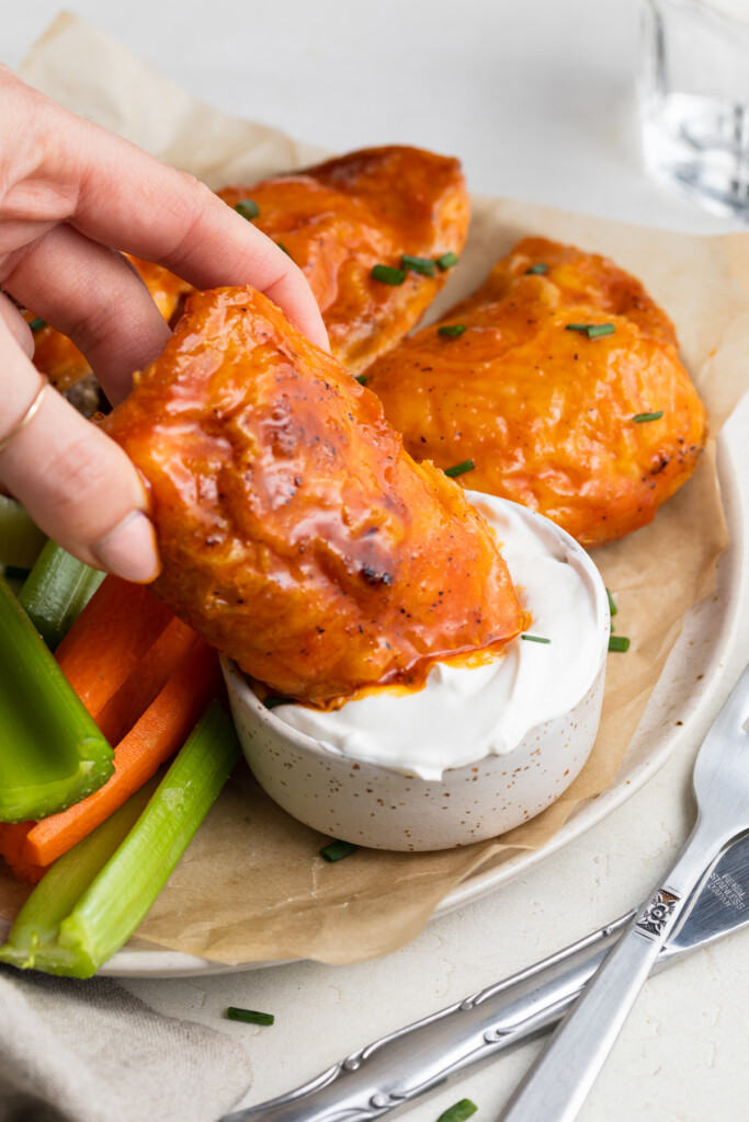 buffalo chicken thighs being dipped into sour cream