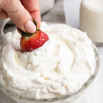 a strawberry being dipped in keto whipped cream