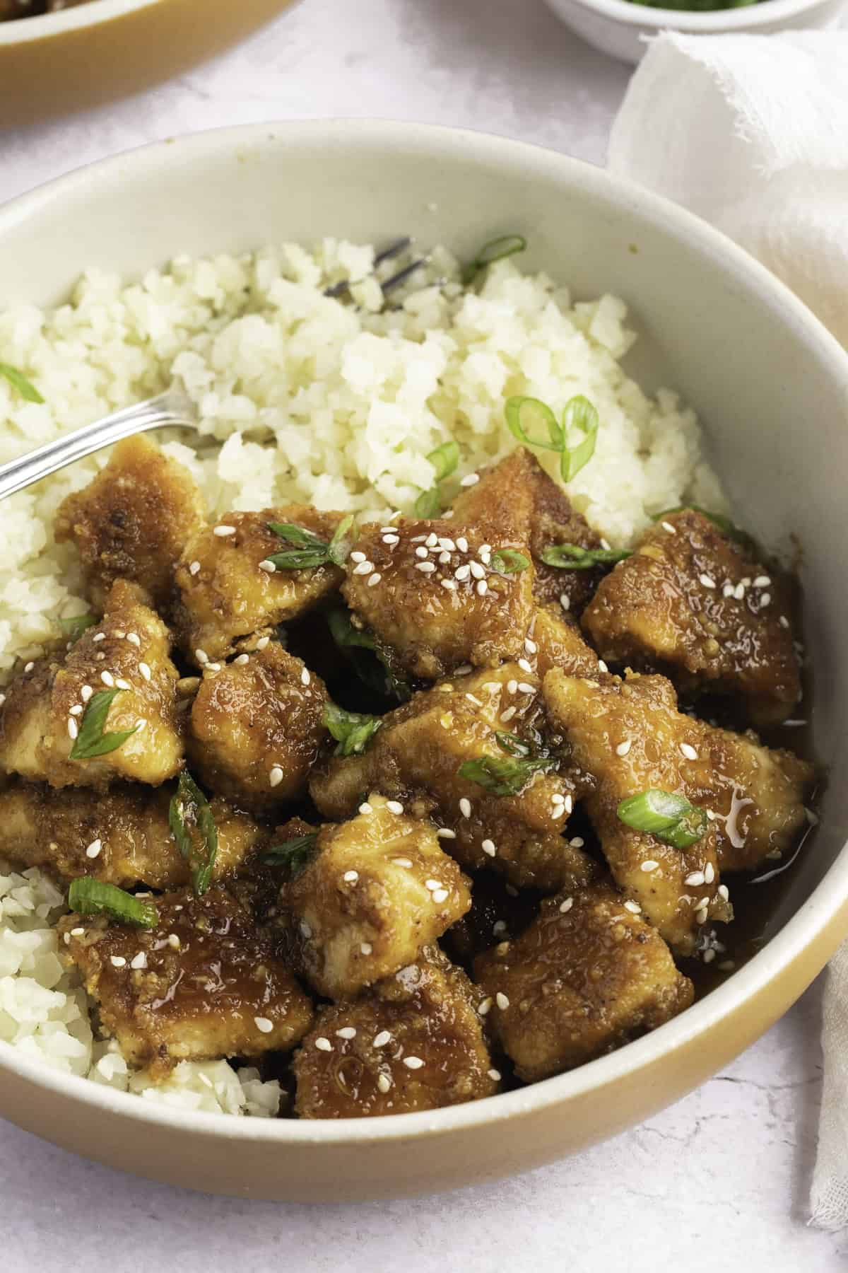 Keto orange chicken with green onions and sesame seeds on a bed of cauliflower rice