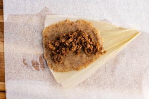Corn husk with keto masa dough and ground beef filling on parchment paper.