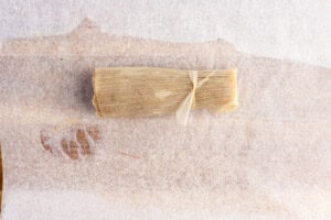 Rolled keto tamale tied with corn husk strip on parchment paper lined cutting board.