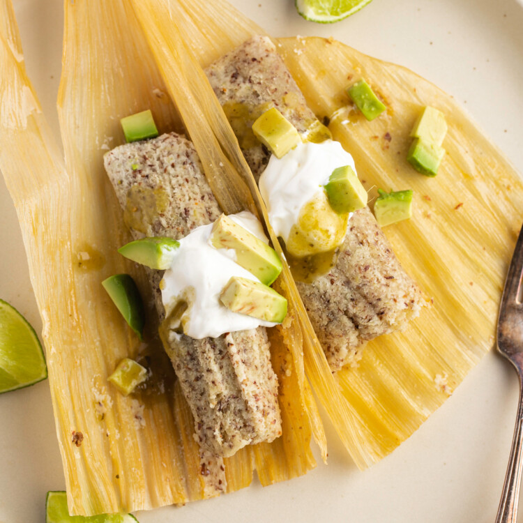 Unwrapped keto tamales with sour cream and avocado on corn husks on a plate.