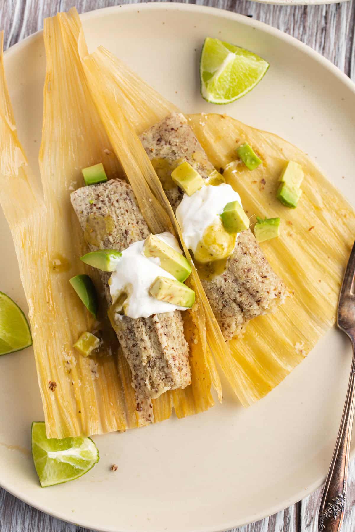 Unwrapped keto tamales with sour cream and avocado on corn husks on a plate.