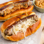 Instant Pot brats on hot dog buns with sauerkraut, on a parchment paper covered tray.
