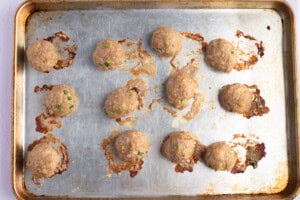 Overhead view of fully-cooked Asian turkey meatballs on a lightly greased baking sheet.