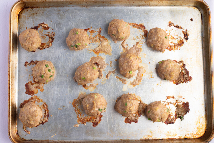Overhead view of fully-cooked Asian turkey meatballs on a lightly greased baking sheet.
