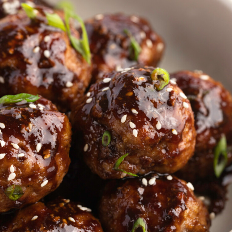 Close-up view of a bowl of Asian turkey meatballs garnished with sesame seeds and green onions.