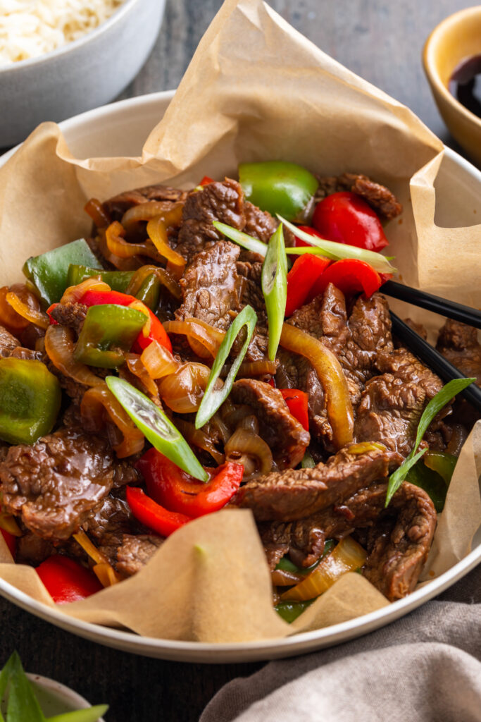 Beef with veggies and oyster sauce in a large silver bowl with parchment paper.