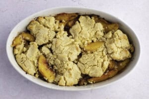 Baked keto peach cobbler in large white oval baking dish.