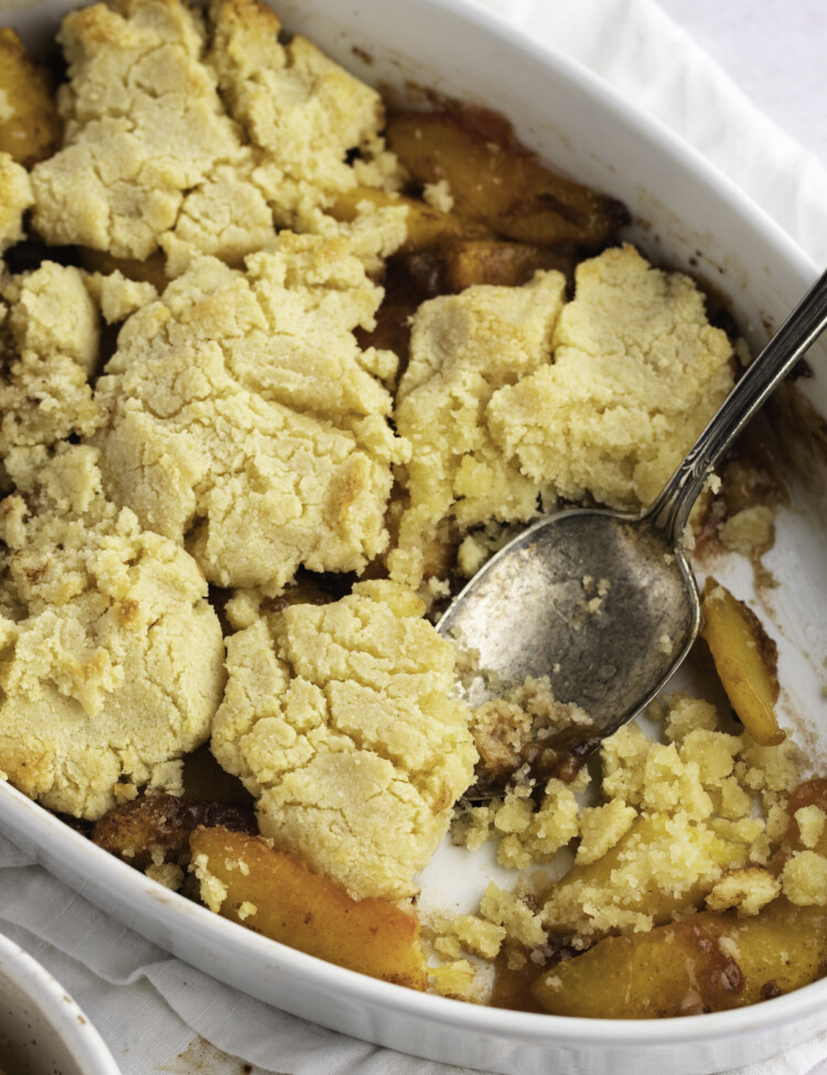 Overhead view of an angled casserole dish holding keto peach cobbler with a large silver spoon.