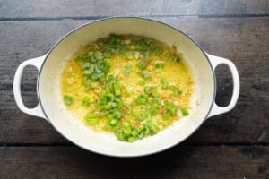 Overhead view of a large soup pot containing green onion and melted butter.