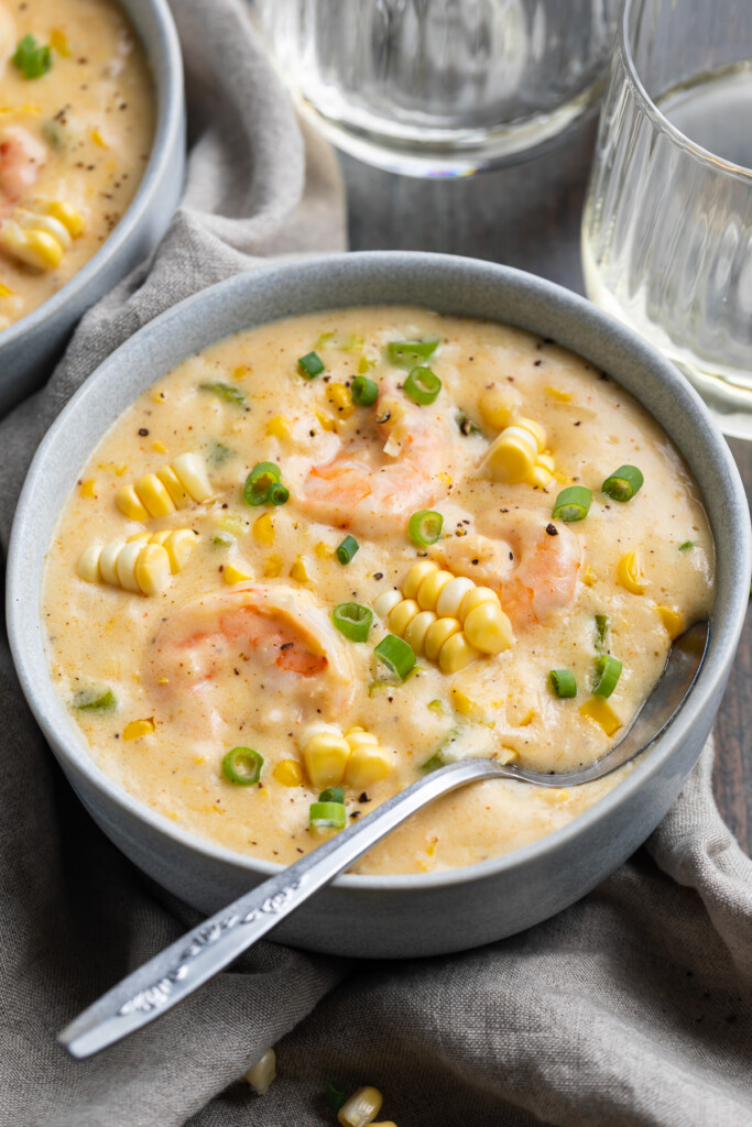 3/4 angle view of a white bowl containing shrimp and corn soup on a neutral cloth napkin.