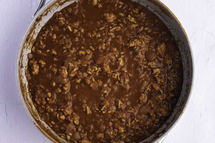 Overhead view of ground turkey and spaghetti sauce in a large skillet on a white background.