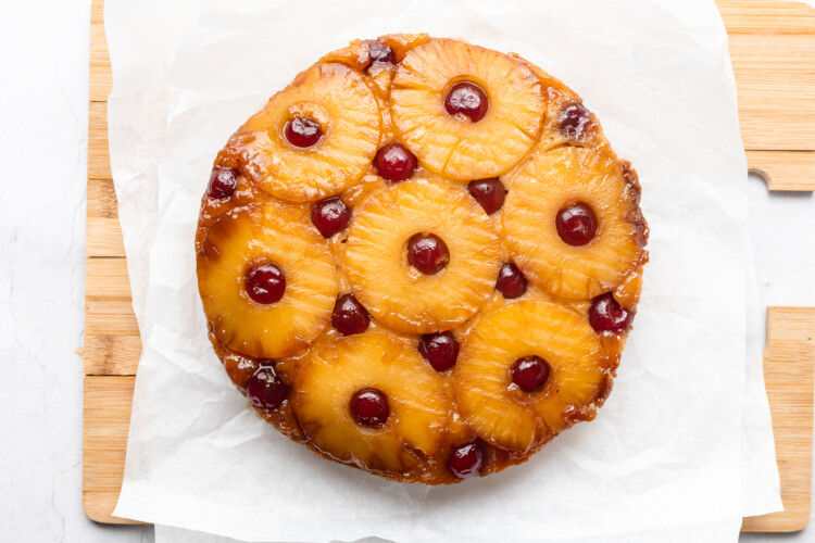 Round pineapple upside-down cake on parchment paper sitting on cutting board.