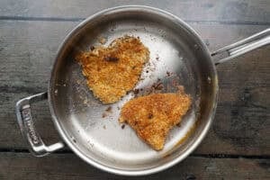 Overhead view of two breaded steaks in a pan with fry oil.