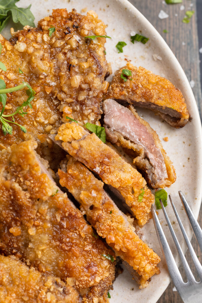 Overhead view of crispy beef schnitzel, sliced thin, with one piece on its side to show the meat.