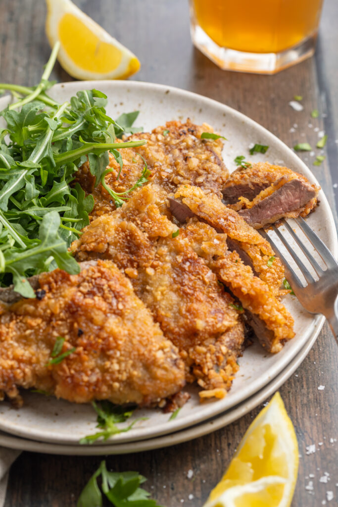 Overhead, angled, zoomed out view of crispy beef schnitzel plated with a salad of microgreens.