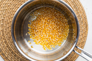 Overhead view of unpopped popcorn kernels in a large silver pot on a wicker placemat.
