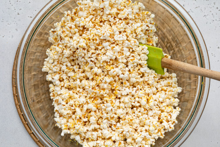 Overhead view of vegan buttery popcorn in a large silver bowl with a rubber spatula.