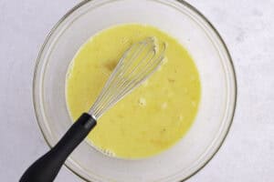 Whisked eggs, milk, salt, and pepper in a large glass mixing bowl with whisk.