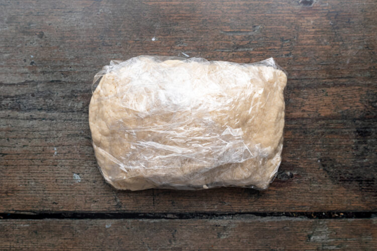 Overhead view of a large block of vegan empanada dough wrapped in plastic wrap.