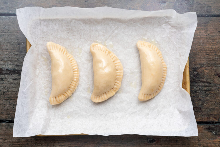 Overhead view of 3 vegan empanadas on a baking sheet lined with parchment paper.