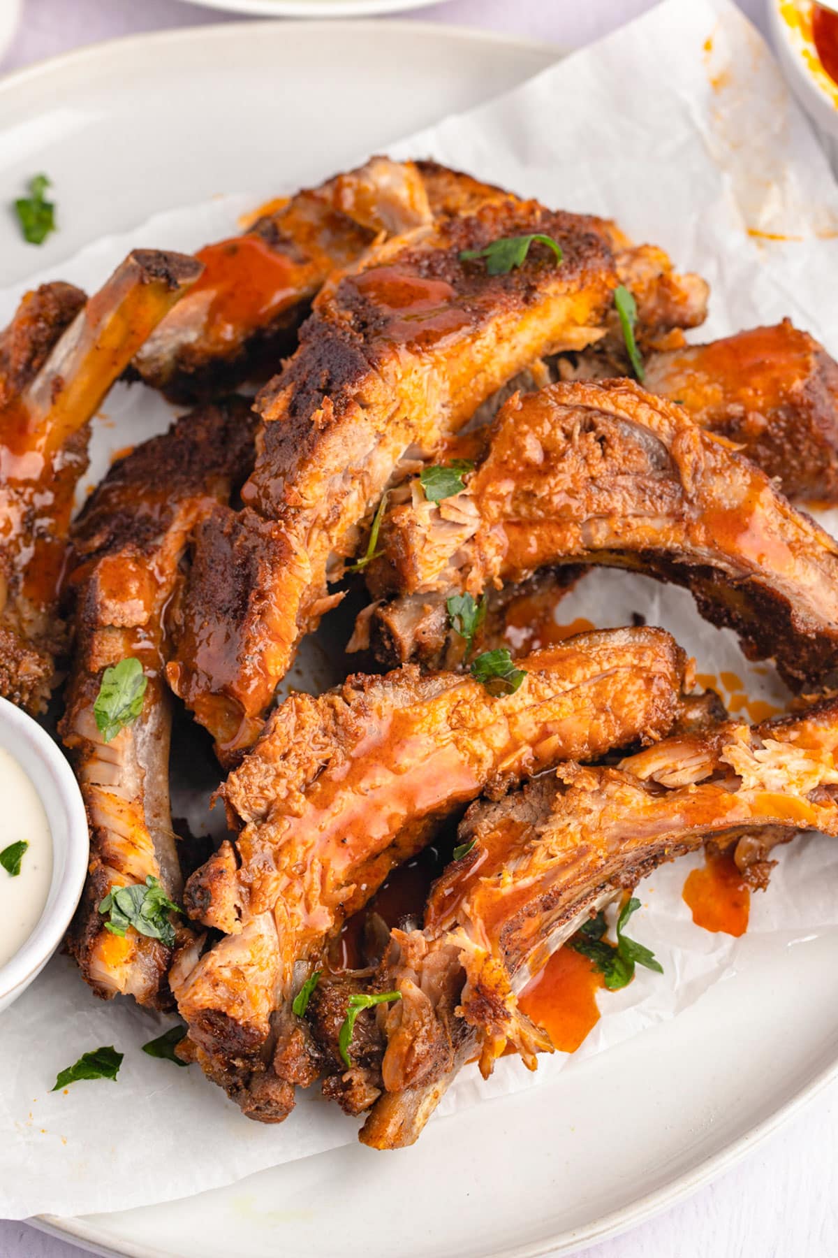 A pile of baked buffalo ribs with bbq sauce on a white plate.