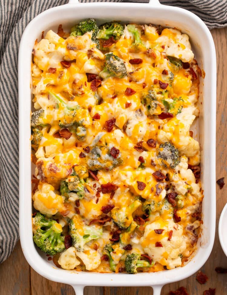 Overhead photo of a large white rectangular casserole dish holding a baked keto broccoli cauliflower casserole topped with lots of cheese and pieces of bacon.