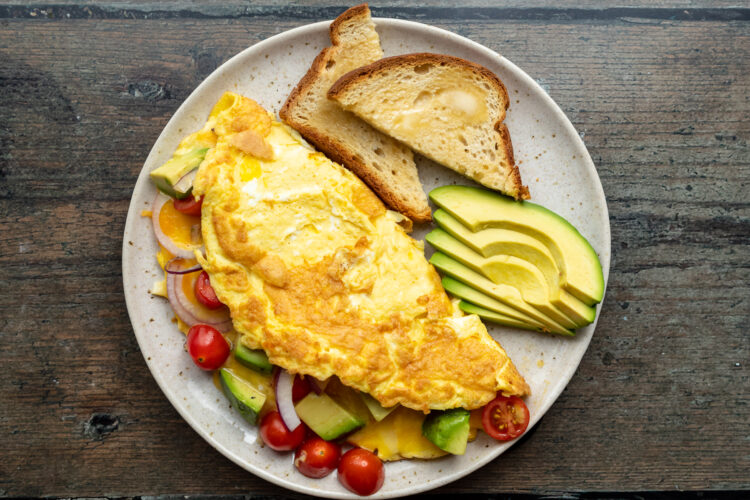 Overhead view of an avocado omelette folded on a white plate with additional tomatoes and avocado.