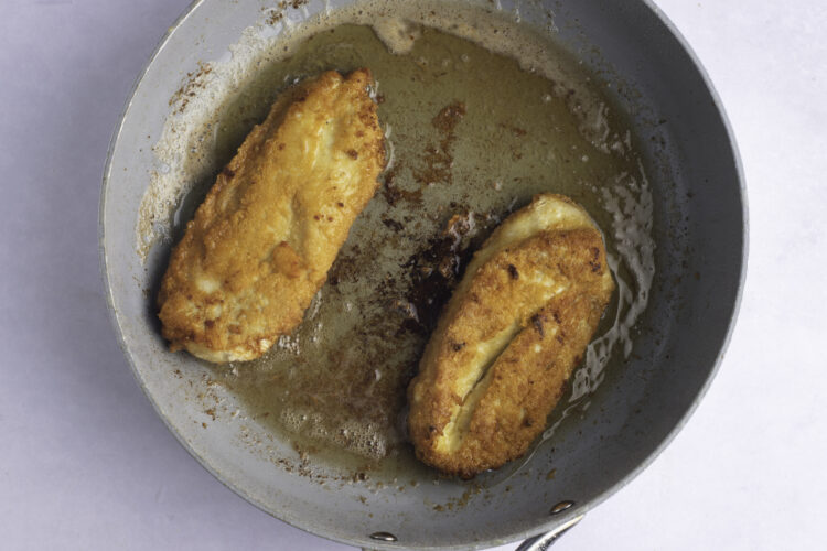 Overhead view of two fried chicken cutlets in a large skillet.