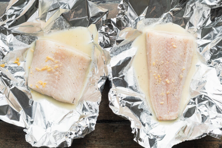 Overhead view of two cod fillets in foil packets with lemon-butter sauce.