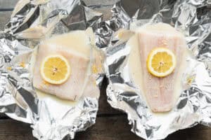 Overhead view of two cod fillets in foil packets with lemon-butter sauce and lemon coins.