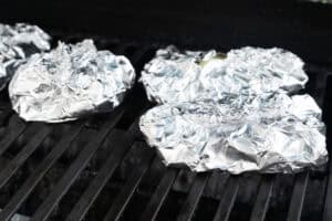 Cod fillets wrapped tightly in aluminum foil packets on a grill over indirect heat.