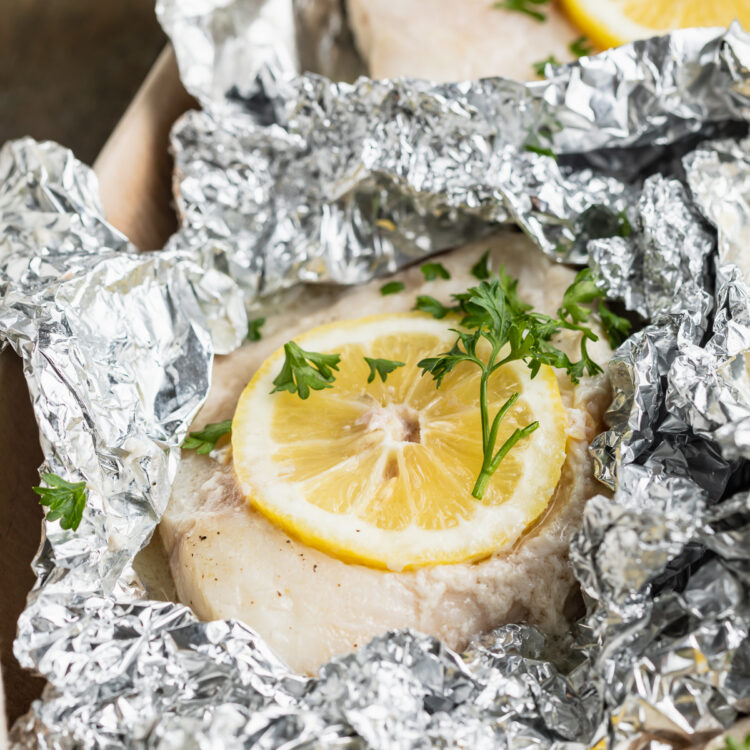 Grilled cod fillet in a foil pouch with lemon discs and fresh herbs.