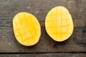 Overhead view of halved and scored mangoes on a baking sheet.